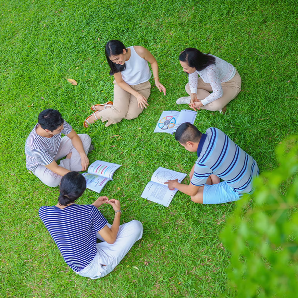 overhead-view-of-five-people-sitting-in-a-circle-on-the-grass-studying-together